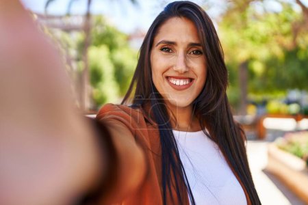 Foto de Joven mujer hispana sonriendo confiada haciendo selfie por la cámara en el parque - Imagen libre de derechos