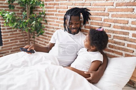 Photo for Father and daughter watching movie sitting on bed at bedroom - Royalty Free Image