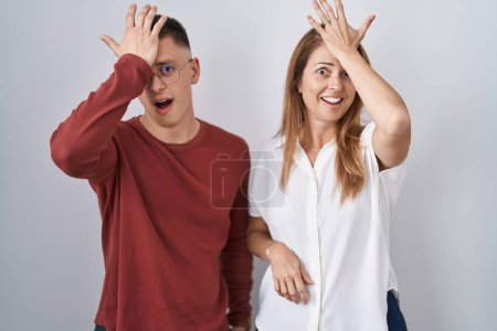 Foto de Mother and son standing together over isolated background surprised with hand on head for mistake, remember error. forgot, bad memory concept. - Imagen libre de derechos