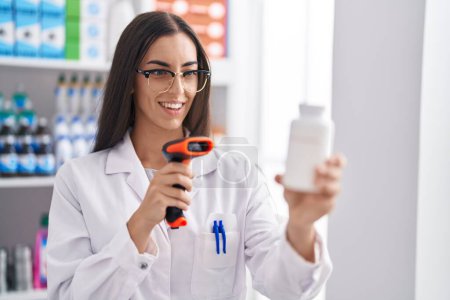 Foto de Joven hermosa mujer hispana farmacéutico escaneo píldoras botella en la farmacia - Imagen libre de derechos