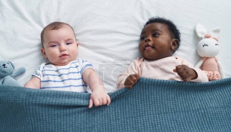 Téléchargez les photos : Deux adorables bébés souriants confiants allongés sur le lit dans la chambre - en image libre de droit