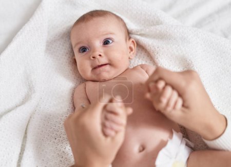 Téléchargez les photos : Adorable caucasian baby lying on bed with holding mother hands at bedroom - en image libre de droit