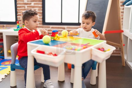 Téléchargez les photos : Deux enfants jouent avec des blocs de construction assis sur la table à la maternelle - en image libre de droit