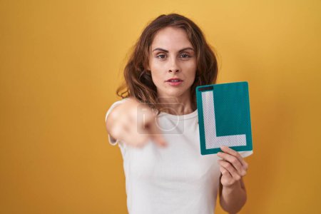 Photo for Beautiful brunette woman holding l sign for new driver pointing with finger to the camera and to you, confident gesture looking serious - Royalty Free Image