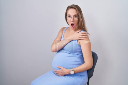 Photo for Young pregnant woman wearing band aid for vaccine injection scared and amazed with open mouth for surprise, disbelief face - Royalty Free Image