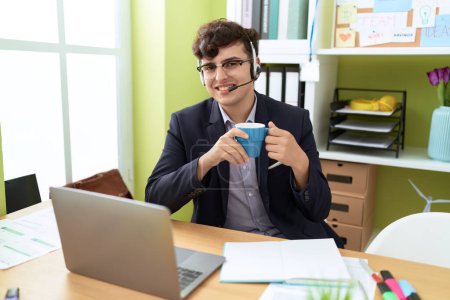 Téléchargez les photos : Non binary man call center agent drinking coffee working at office - en image libre de droit