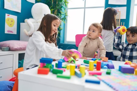 Foto de Grupo de niños jugando con bloques de construcción sentados en la mesa en el jardín de infantes - Imagen libre de derechos