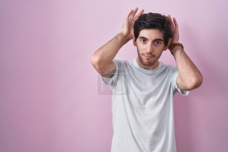 Photo for Young hispanic man standing over pink background doing bunny ears gesture with hands palms looking cynical and skeptical. easter rabbit concept. - Royalty Free Image