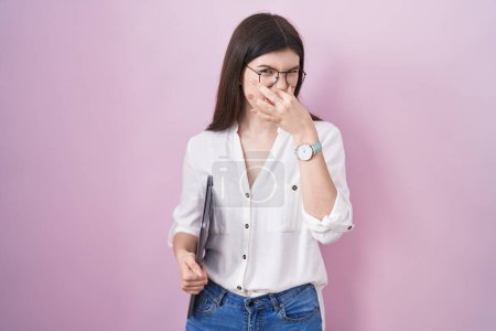 Téléchargez les photos : Jeune femme caucasienne tenant un ordinateur portable sentant quelque chose de puant et dégoûtant, odeur intolérable, retenant souffle avec les doigts sur le nez. mauvaise odeur - en image libre de droit