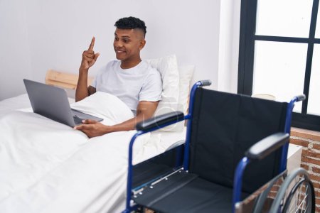 Photo for Young hispanic man lying on the bed, using wheelchair smiling with an idea or question pointing finger with happy face, number one - Royalty Free Image