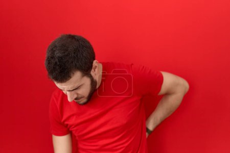 Photo for Young hispanic man wearing casual red t shirt suffering of backache, touching back with hand, muscular pain - Royalty Free Image