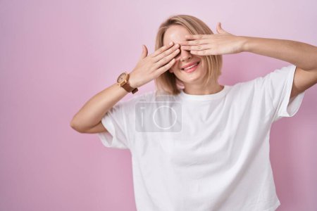 Téléchargez les photos : Jeune femme caucasienne debout sur fond rose couvrant les yeux avec les mains souriantes gaies et drôles. concept aveugle. - en image libre de droit