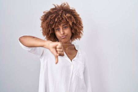 Foto de Young hispanic woman with curly hair standing over white background looking unhappy and angry showing rejection and negative with thumbs down gesture. bad expression. - Imagen libre de derechos