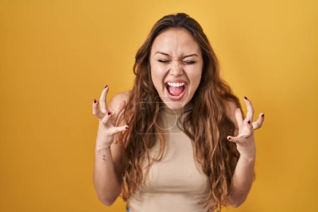 Foto de Young hispanic woman standing over yellow background celebrating mad and crazy for success with arms raised and closed eyes screaming excited. winner concept - Imagen libre de derechos