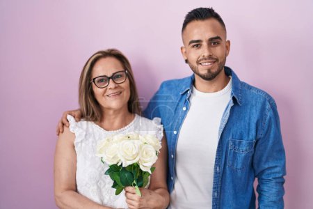 Téléchargez les photos : Mère hispanique et fils tenant ensemble un bouquet de fleurs blanches souriant avec un sourire heureux et frais sur le visage. montrant les dents. - en image libre de droit