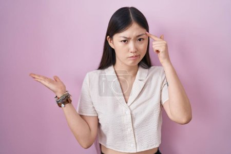 Téléchargez les photos : Chinese young woman standing over pink background confused and annoyed with open palm showing copy space and pointing finger to forehead. think about it. - en image libre de droit
