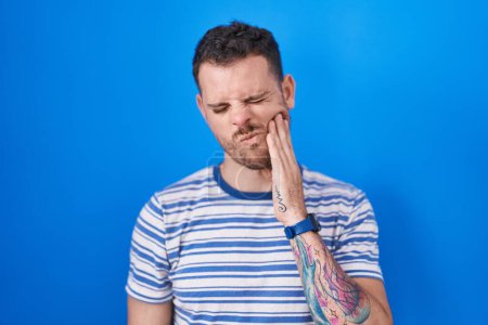 Photo for Young hispanic man standing over blue background touching mouth with hand with painful expression because of toothache or dental illness on teeth. dentist - Royalty Free Image