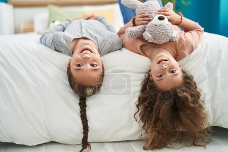 Foto de Two kids holding teddy bear lying on bed at bedroom - Imagen libre de derechos