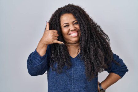 Téléchargez les photos : Plus size hispanic woman standing over white background smiling doing phone gesture with hand and fingers like talking on the telephone. communicating concepts. - en image libre de droit
