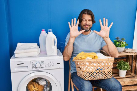 Téléchargez les photos : Bel homme d'âge moyen attendant la lessive montrant et pointant vers le haut avec les doigts numéro dix tout en souriant confiant et heureux. - en image libre de droit