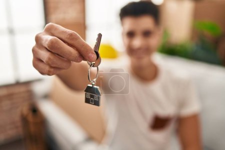 Téléchargez les photos : Jeune homme hispanique souriant confiant tenant la clé de la maison à la nouvelle maison - en image libre de droit