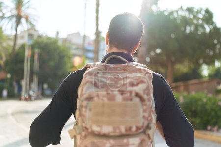 Téléchargez les photos : Jeune homme hispanique portant un sac à dos marchant dans la rue - en image libre de droit