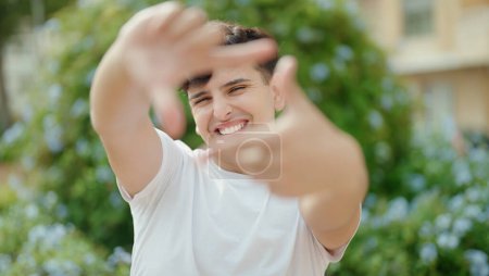 Foto de Hombre no binario sonriendo confiado haciendo gesto fotográfico con las manos en el parque - Imagen libre de derechos