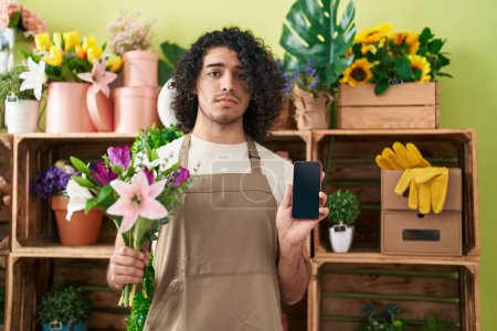 Photo for Hispanic man with curly hair working at florist shop showing smartphone screen depressed and worry for distress, crying angry and afraid. sad expression. - Royalty Free Image