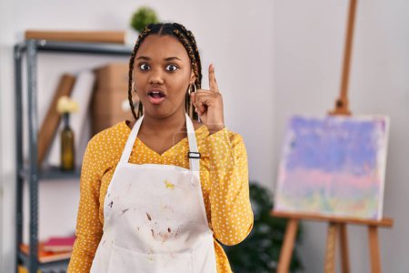Téléchargez les photos : Femme afro-américaine avec des tresses au studio d'art pointant du doigt avec une idée réussie. Sorti et heureux. numéro un. - en image libre de droit