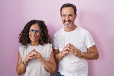 Téléchargez les photos : Couple hispanique du Moyen Âge ensemble sur fond rose mains ensemble et doigts croisés souriant détendu et joyeux. succès et optimisme - en image libre de droit