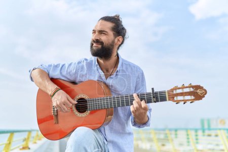 Téléchargez les photos : Jeune musicien hispanique jouant de la guitare classique au bord de la mer - en image libre de droit