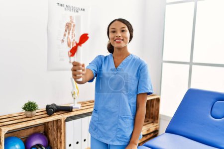Photo for Young latin woman wearing physiotherapist uniform holding diploma at clinic - Royalty Free Image