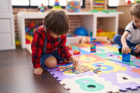 Téléchargez les photos : Deux enfants jouant avec des blocs de construction et des mathématiques jeu de puzzle assis sur le sol à la maternelle - en image libre de droit