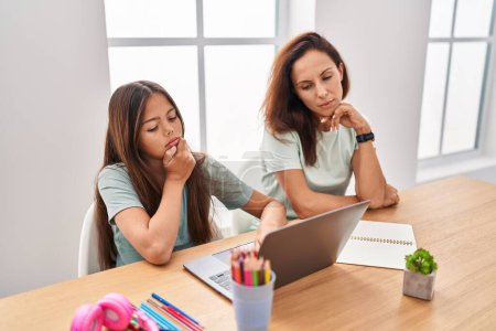 Photo for Young mother and daughter doing homework at home serious face thinking about question with hand on chin, thoughtful about confusing idea - Royalty Free Image