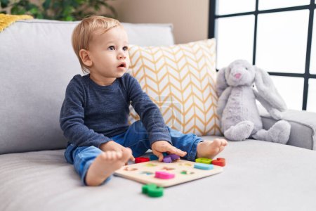 Téléchargez les photos : Adorable tout-petit blond jouant avec les mathématiques jeu assis sur le canapé à la maison - en image libre de droit