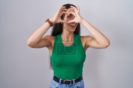 Photo for Young woman standing over isolated background doing heart shape with hand and fingers smiling looking through sign - Royalty Free Image
