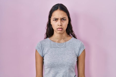 Foto de Mujer brasileña joven con camiseta casual sobre fondo rosa escéptico y nervioso, frunciendo el ceño molesto debido a un problema. persona negativa. - Imagen libre de derechos