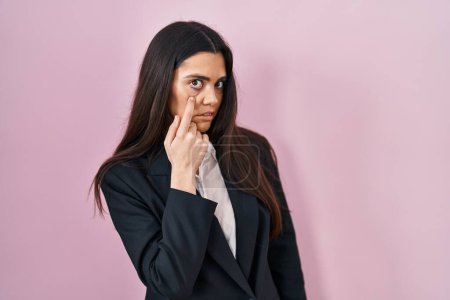 Foto de Young brunette woman wearing business style over pink background pointing to the eye watching you gesture, suspicious expression - Imagen libre de derechos