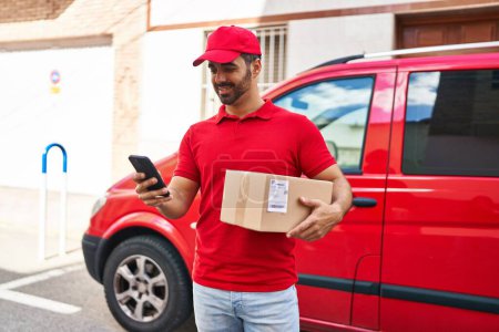 Photo for Young hispanic man courier using smartphone holding package at street - Royalty Free Image