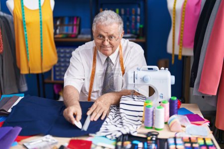 Téléchargez les photos : Middle age grey-haired man tailor smiling confident make mark on cloth at tailor shop - en image libre de droit