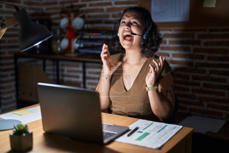 Photo for Young hispanic woman working at the office at night crazy and mad shouting and yelling with aggressive expression and arms raised. frustration concept. - Royalty Free Image