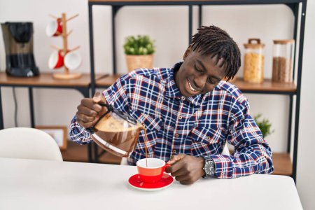 Foto de African american man pouring coffee on cup sitting on table at home - Imagen libre de derechos