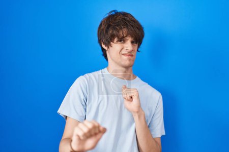 Photo for Hispanic young man standing over blue background disgusted expression, displeased and fearful doing disgust face because aversion reaction. - Royalty Free Image