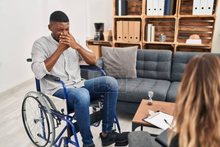 Téléchargez les photos : Homme afro-américain faisant une thérapie assis sur fauteuil roulant sentant quelque chose de puant et dégoûtant, odeur intolérable, retenant souffle avec les doigts sur le nez. mauvaise odeur - en image libre de droit