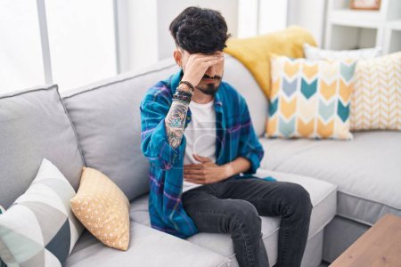 Foto de Joven hispano sufriendo de dolor de estómago sentado en el sofá en casa - Imagen libre de derechos