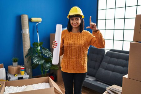 Photo for Young hispanic woman standing on new home with blueprints surprised with an idea or question pointing finger with happy face, number one - Royalty Free Image