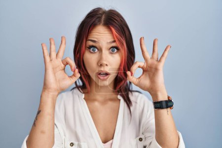 Photo for Young caucasian woman wearing casual white shirt over isolated background looking surprised and shocked doing ok approval symbol with fingers. crazy expression - Royalty Free Image