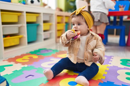 Foto de Adorable niño rubio sentado en el suelo chupando juguete en el jardín de infantes - Imagen libre de derechos