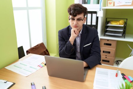 Téléchargez les photos : Homme non binaire travailleur d'affaires en utilisant un ordinateur portable avec une expression détendue au bureau - en image libre de droit