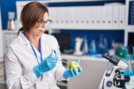 Foto de Mujer de mediana edad científica inyectando líquido en manzana en el laboratorio - Imagen libre de derechos